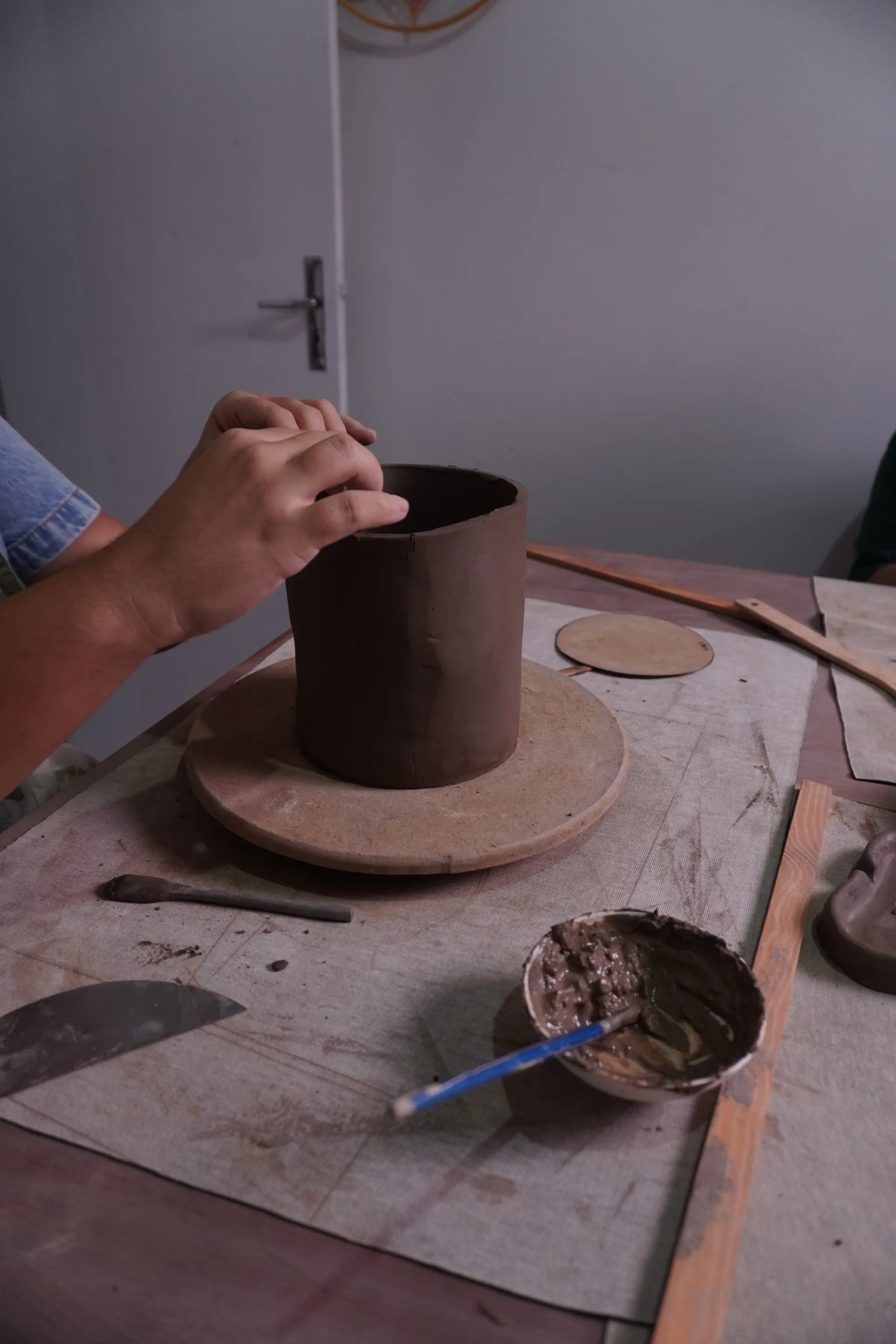 Mãos ajustando a borda de uma forma cilíndrica de argila